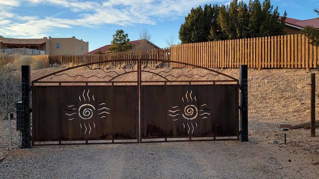 Rustic metal gate with decorative sun design, leading to a gravel driveway.
