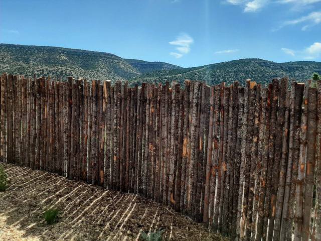 Brown log fence with mountains in the background under a blue sky.