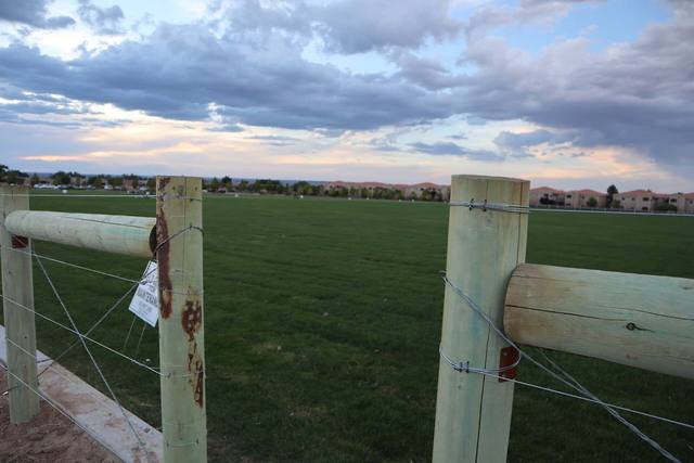 Wooden fence bordering a green field under a cloudy sky.