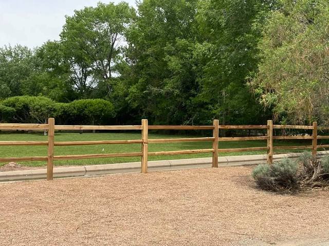 Wooden split-rail fence in front of a grassy area, with trees in the background.
